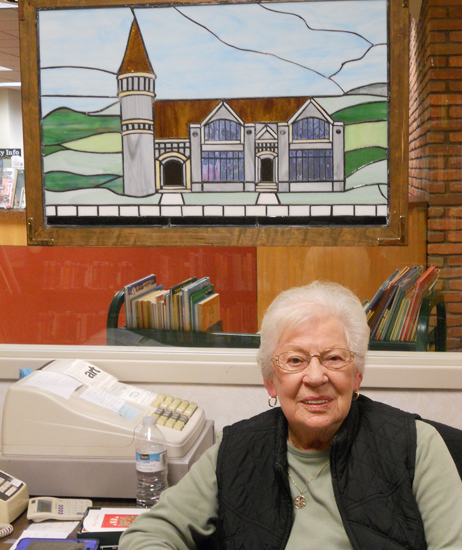 Older woman sitting at register and smiling while working in the library bookstore