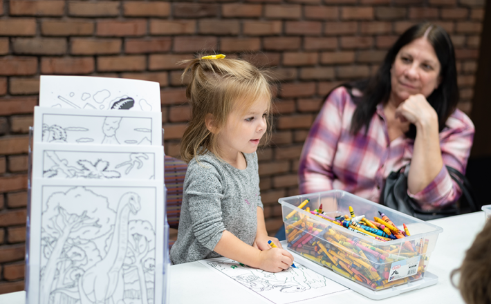 Young girl coloring while woman looks at her